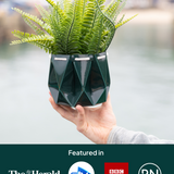Self watering Ocean Plant Pot held by a person, featuring green foliage and a unique origami design.